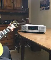 A person playing guitar in front of a table with a clock.